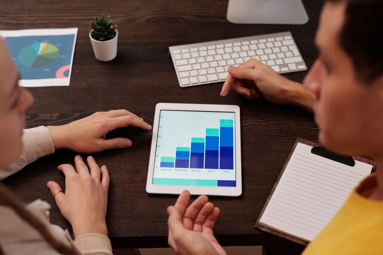 heros-img Team members discussing digital graphs on a tablet in a modern office setting.